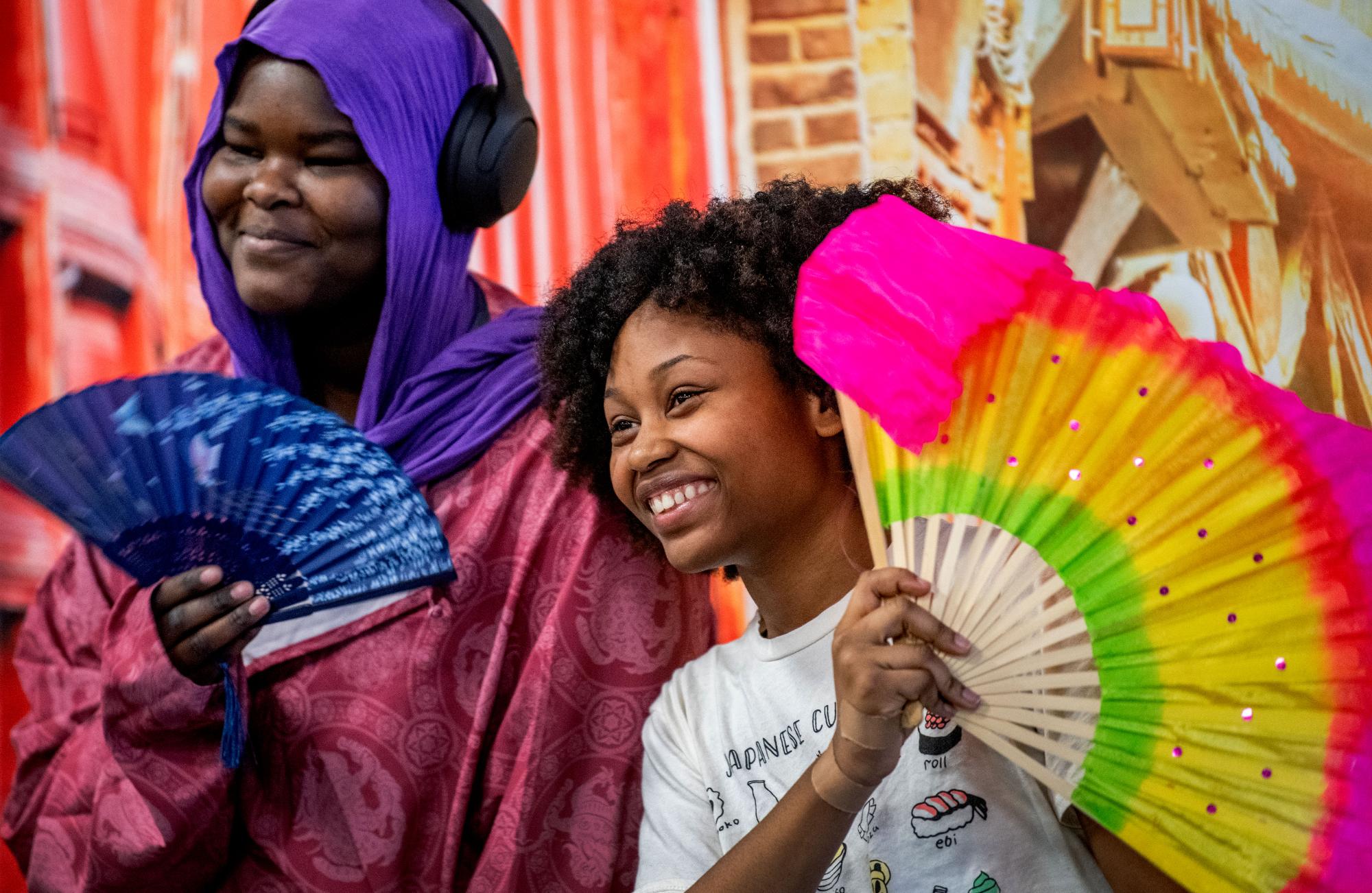 Two young people smiling and holding colorful fans